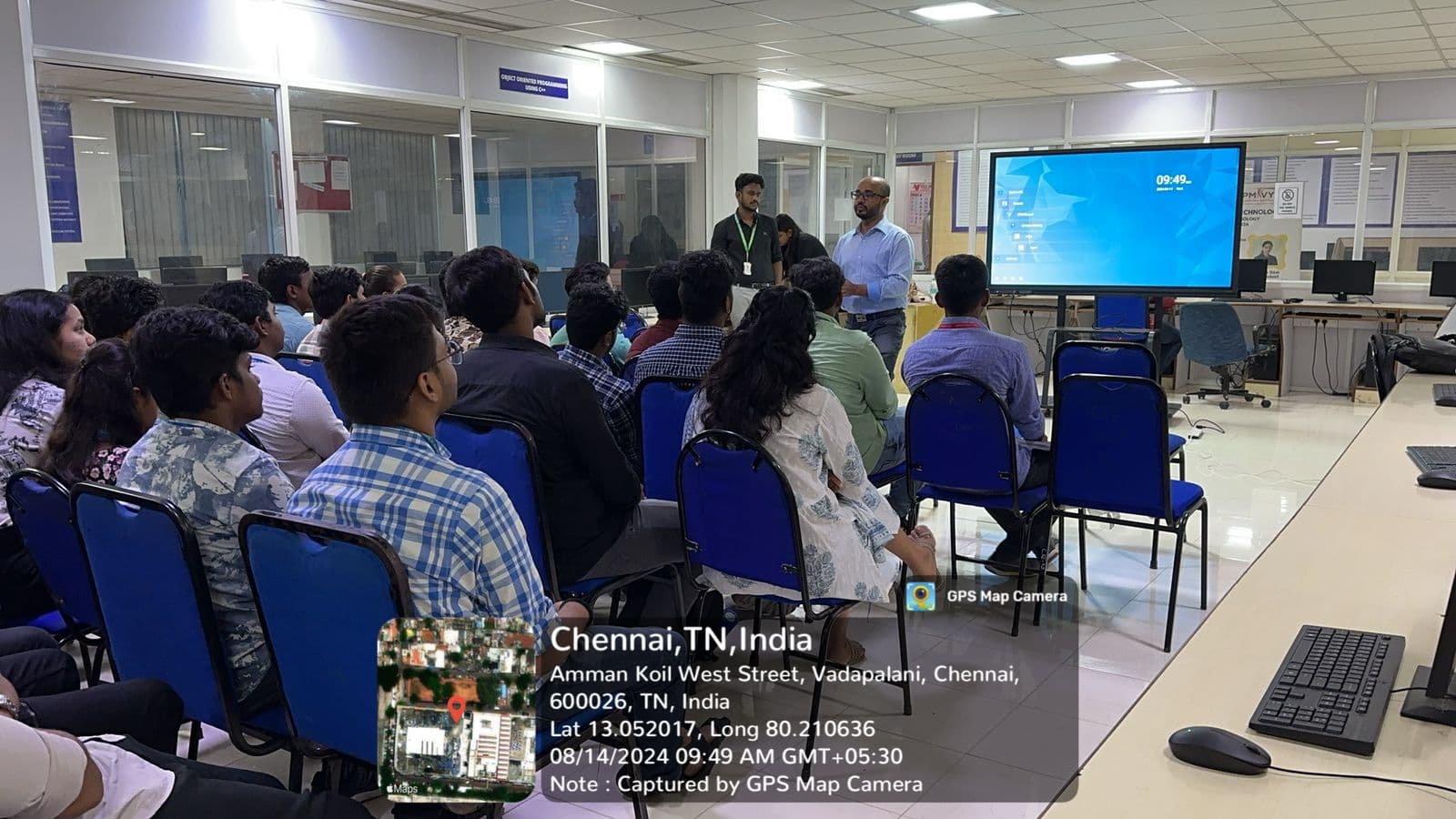 The workshop audience seated in rows of blue chairs facing the screen, a speaker standing at the front of the lab.